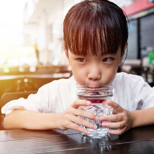 Child drinking safe water from glass cup